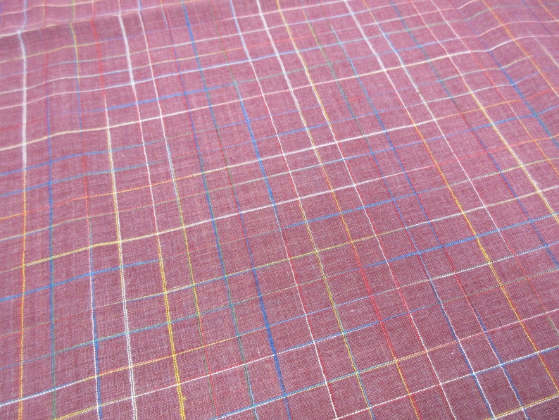 May include: A close-up of a red fabric with a multi-coloured plaid pattern. The fabric has white, blue, yellow, and red stripes.