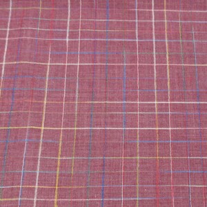 May include: A close-up of a red fabric with a multi-coloured plaid pattern. The fabric has a subtle texture and a slightly faded appearance.
