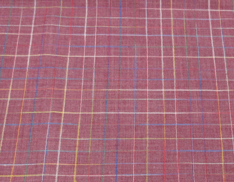 May include: A close-up of a red fabric with a multi-coloured plaid pattern. The fabric has a subtle texture and a slightly faded appearance.