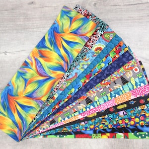 May include: A collection of 15 colorful fabric strips with various patterns, including abstract swirls, floral designs, and geometric shapes. The fabric strips are arranged in a fan shape, with the largest strip at the top and the smallest strip at the bottom.