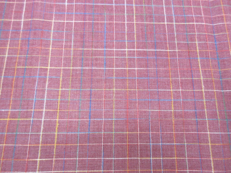 May include: A close-up of a red fabric with a multi-coloured plaid pattern. The fabric has a subtle texture and a soft, woven appearance.