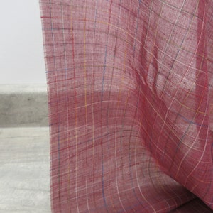 May include: A close-up of a red fabric with a checkered pattern. The fabric has thin white, yellow, and blue lines woven into the red fabric.