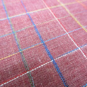 May include: Close-up of a red fabric with a checkered pattern. The fabric has white, blue, yellow, and red lines.