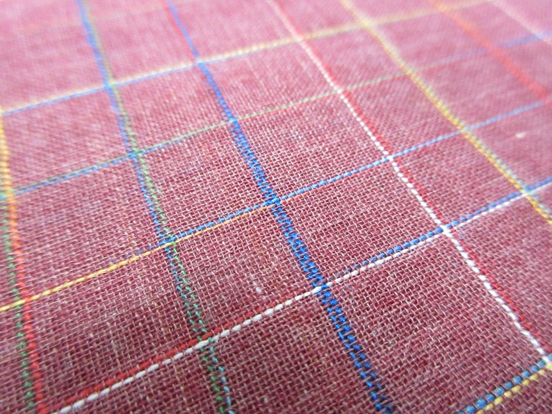 May include: Close-up of a red fabric with a checkered pattern. The fabric has white, blue, yellow, and red lines.
