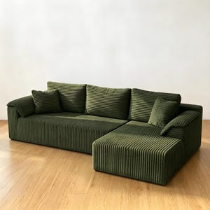 May include: A dark olive green sectional sofa upholstered in a textured corduroy fabric. The sofa features a low-profile design with a chaise lounge section on the right, three large back cushions, and two smaller square throw pillows.