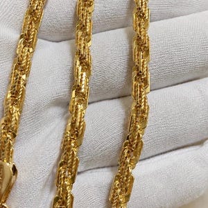 May include: A gold chain necklace featuring a complex, multi-link design with alternating smooth, rectangular segments and twisted, rope-like sections. The metallic yellow finish has a high-shine, reflective surface throughout the entire length.