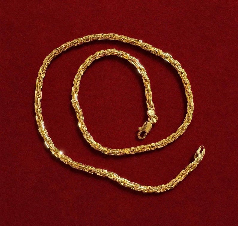 May include: A gold chain necklace featuring a textured, interlocking link design. The chain is arranged in a circular pattern and includes a secure lobster claw clasp mechanism at one end, showcasing a polished, reflective metallic finish throughout.