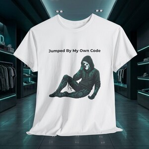 Puede incluir: Una camiseta blanca de manga corta con el gráfico de una figura encapuchada con un traje oscuro y patrones de circuitos en color verde azulado, sentada y cubriéndose la cara. El texto "Jumped By My Own Code" aparece impreso en negro arriba.