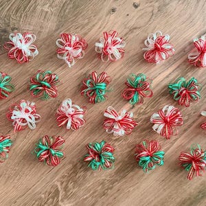 May include: A collection of twenty-three small, decorative bows made from thin, translucent ribbon. The bows feature a mix of red, white, and green striped patterns, arranged in a circular, multi-looped design with frayed, wispy edges.