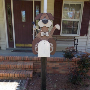May include: A wooden dog mailbox with a brown and white paint scheme. The mailbox is shaped like a dog with a name tag that reads "Duke".
