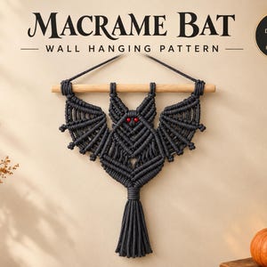 May include: A dark gray macrame bat wall hanging suspended from a light wooden dowel. The bat features intricate knotted cord wings, pointed ears, and two small red beads for eyes. The text reads MACRAME BAT WALL HANGING PATTERN and DIGITAL PDF PATTERN.