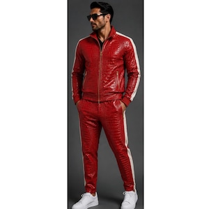 Peut inclure: Un survêtement rouge avec un motif texturé en peau de crocodile. La veste présente une fermeture éclair dorée intégrale, un col montant et des bandes latérales blanches. Le pantalon assorti inclut des bandes latérales blanches.