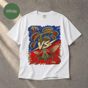 Może przedstawiać: Biały t-shirt z krótkim rękawem z nadrukiem graficznym przedstawiającym muchołówkę kontra muchę. Wzór zawiera napis "Venus Fly Trap" u góry i "Fly" u dołu, oddzielone dużym "VS" pośrodku, na niebieskim i czerwonym tle.