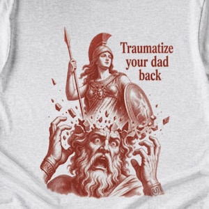 May include: A light gray t-shirt featuring a red graphic illustration of a warrior figure holding a spear and shield above a man with a distressed expression. The text "Traumatize your dad back" is printed in red to the right of the warrior figure.