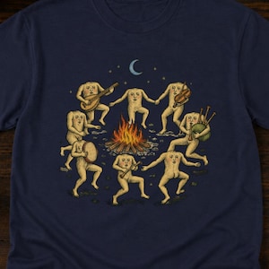 May include: A navy blue t-shirt featuring a graphic illustration of seven pale, headless figures dancing in a circle around a campfire. The figures are playing various musical instruments including a lute, violin, bagpipes, and a tambourine.
