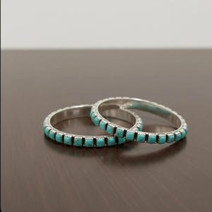 Puede incluir: Dos brazaletes de plata con incrustaciones de peque&ntilde;as piedras de turquesa de corte cuadrado. Cada pulsera tiene un acabado de metal pulido y una hilera continua de piedras de color azul verdoso engastadas alrededor de toda la banda.