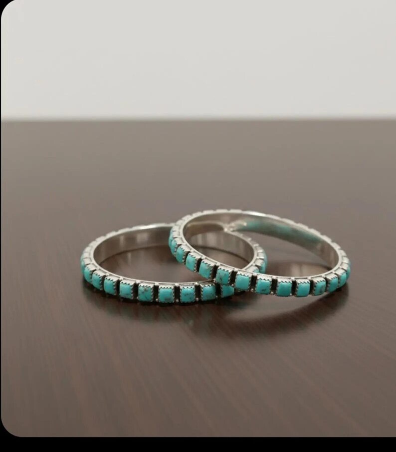 Puede incluir: Dos brazaletes de plata con incrustaciones de peque&ntilde;as piedras de turquesa de corte cuadrado. Cada pulsera tiene un acabado de metal pulido y una hilera continua de piedras de color azul verdoso engastadas alrededor de toda la banda.