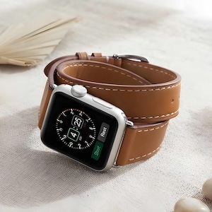 May include: A silver smartwatch with a rectangular screen displaying a digital clock face showing 4:25 and the word Rest. The watch features a long, tan leather double-wrap band with white contrast stitching and a silver metal buckle closure.