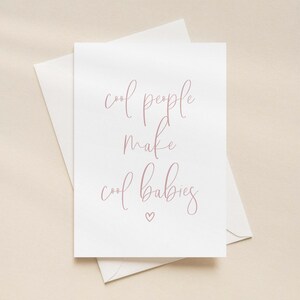 以下が含まれることがあります： ダスティローズ色の筆記体フォントで「cool people make cool babies」というテキストが書かれた白いグリーティングカード。テキストの下には小さなハートのシンボルがあり、お揃いの白い封筒の上に置かれています。