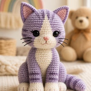 May include: A crocheted cat toy featuring light purple yarn with darker purple stripes on the head, back, and tail. The cat has a white chest, face, and paws, large black plastic eyes, a small pink stitched nose, and black thread whiskers.