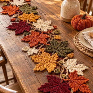 Può includere: Un runner da tavola all'uncinetto caratterizzato da una serie di foglie d'acero interconnesse nei toni del rosso scuro, arancione bruciato, giallo oro, verde oliva e crema. Le foglie sono collegate da un sottile cordoncino a uncinetto.