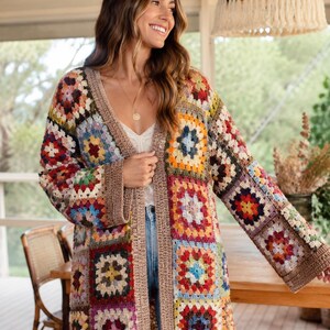 Può includere: Un cardigan a maniche lunghe realizzato con toppe all'uncinetto a motivi granny square multicolori. Il capo presenta uno scollo a V e un ampio bordo a coste marrone tinta unita lungo l'apertura frontale e i polsini, con colori vivaci.