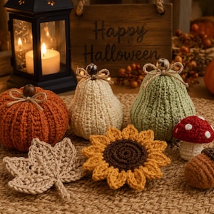 Op de afbeelding: Een verzameling gehaakte herfstdecoraties waaronder een roestoranje pompoen, een crèmekleurige peer, een saliegroene peer, een beige esdoornblad, een gele zonnebloem, een rood-witte paddenstoel en een bruine eikel met touwstrikjes.