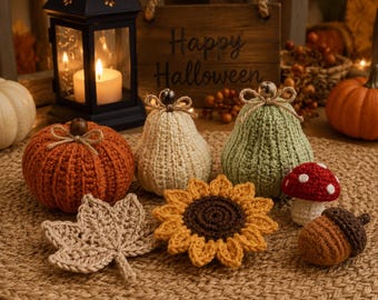 May include: A collection of crocheted autumn decorations including a burnt orange pumpkin, a cream pear, a sage green pear, a beige maple leaf, a yellow sunflower, a red and white mushroom, and a brown acorn, all featuring twine bows.