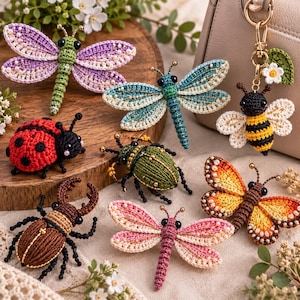 Könnte beinhalten: Eine Sammlung gehäkelter Insektenornamente, darunter eine violette Libelle, eine blaue Libelle, ein Marienkäfer, ein grüner Käfer, ein brauner Hirschkäfer, eine rosa Libelle, ein Monarchfalter und ein Bienen-Schlüsselanhänger mit Blume.