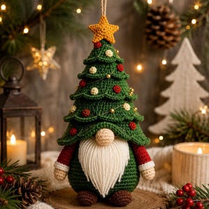 Pode incluir: Uma figura de gnomo em crochê com um chapéu em forma de árvore verde, rematado por uma estrela amarela, decorado com pequenas esferas vermelhas e brancas e fio dourado. O gnomo tem um nariz bege, uma longa barba de lã branca, mangas vermelhas e pés castanhos.