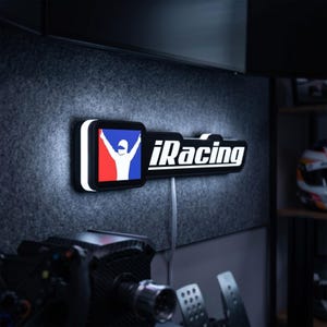 May include: A rectangular wall-mounted LED sign featuring the iRacing logo in white text next to a square icon of a white driver silhouette against a red and blue background. The sign emits a bright white glow from its edges and includes a power cord.