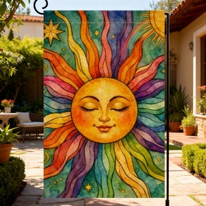 May include: A rectangular garden flag featuring a central sun with a peaceful face, closed eyes, and a gentle smile. The sun is surrounded by vibrant, wavy rays in a rainbow spectrum of colors against a teal background with small yellow stars.