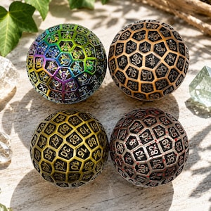 May include: Four spherical dice with a honeycomb lattice structure, each featuring numbers engraved on individual hexagonal facets. The dice are finished in iridescent rainbow, metallic gold, antique brass, and silver with red accents.