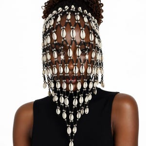 May include: A face veil constructed from a lattice of black beads and metallic silver beads, featuring white cowrie shells integrated into the diamond-shaped pattern. The accessory drapes over the upper face and forehead, creating a structured mesh.