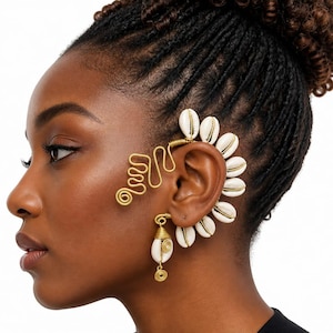 Pode incluir: Um ear cuff de fio metálico dourado com uma série de conchas búzios brancas dispostas ao longo da borda externa da orelha. O design inclui um padrão decorativo de fio em ziguezague em direção à têmpora e um pingente de concha pendurado.