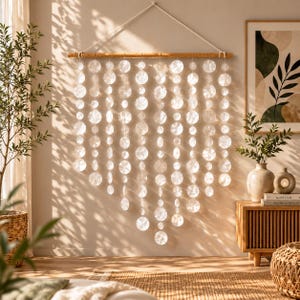 May include: A wall hanging featuring multiple vertical strands of translucent, circular discs suspended from a horizontal wooden rod. The discs are arranged in a V-shaped pattern, creating a layered effect that catches light and casts soft shadows.