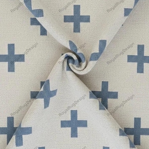 Puede incluir: Una tela tejida con un patrón repetitivo de signos más azules sobre un fondo beige claro. El material está recogido en el centro, creando un pliegue en espiral. El texto RoyalRugDesign está impreso repetidamente en la superficie.