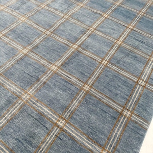 May include: A blue area rug featuring a grid pattern composed of thin white and tan lines. The surface has a textured, woven appearance with visible fibers. The text RoyalRugDesign is repeated across the surface in a light, semi-transparent font.