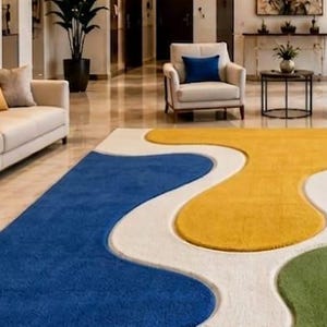 Peut inclure: Un grand tapis pr&eacute;sentant un motif abstrait audacieux avec des formes fluides et organiques dans des tons vifs de bleu, jaune, vert et rouge, sur un fond blanc cr&egrave;me. Le tapis poss&egrave;de une surface textur&eacute;e et recouvre un sol poli.