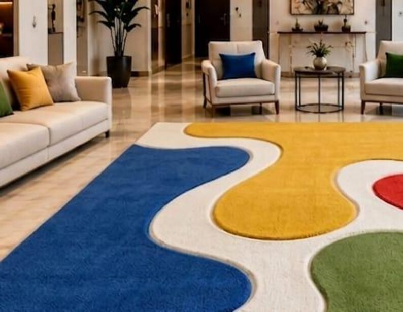 Peut inclure: Un grand tapis pr&eacute;sentant un motif abstrait audacieux avec des formes fluides et organiques dans des tons vifs de bleu, jaune, vert et rouge, sur un fond blanc cr&egrave;me. Le tapis poss&egrave;de une surface textur&eacute;e et recouvre un sol poli.