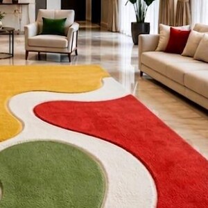 Peut inclure: Un grand tapis pr&eacute;sentant un motif abstrait textur&eacute; et multicolore avec des formes organiques fluides en jaune vif, rouge profond et vert doux, le tout sur un fond blanc cass&eacute; qui recouvre toute la surface du sol.
