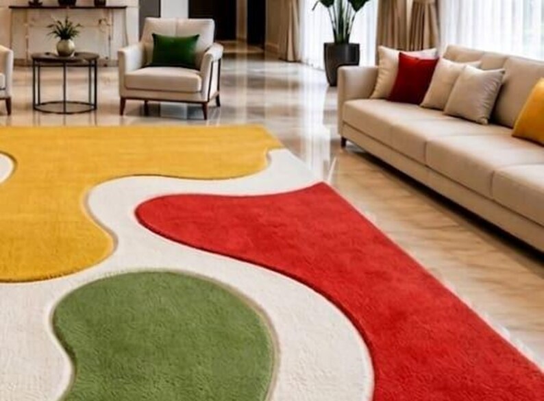 Peut inclure: Un grand tapis pr&eacute;sentant un motif abstrait textur&eacute; et multicolore avec des formes organiques fluides en jaune vif, rouge profond et vert doux, le tout sur un fond blanc cass&eacute; qui recouvre toute la surface du sol.