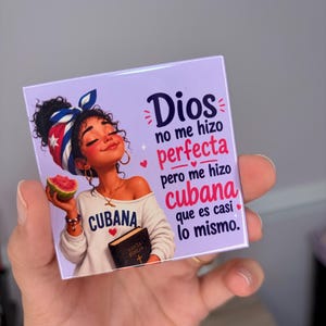 Könnte beinhalten: Ein quadratischer Magnet mit hellviolettem Hintergrund zeigt eine Person mit einem Kopftuch in den Farben der kubanischen Flagge, die ein Stück Wassermelone und ein Buch hält. Der Text lautet: Dios no me hizo perfecta pero me hizo cubana que es casi lo mismo.