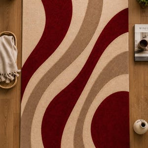 May include: A rectangular area rug featuring a bold, repeating pattern of sweeping, curved bands in deep red, warm beige, and soft tan. The design consists of smooth, flowing lines that create a rhythmic, wave-like visual effect across the entire surface.