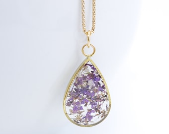 May include: A gold chain necklace with a teardrop-shaped pendant filled with pressed purple flowers.