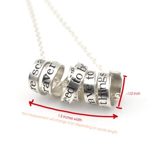 May include: Silver necklace with a spiral of six rings, each engraved with a different phrase. The phrases are "be scared", "braver", "need to be", "have to", "things", and "1". The necklace is 1.5 inches wide and 1/2 inch thick.