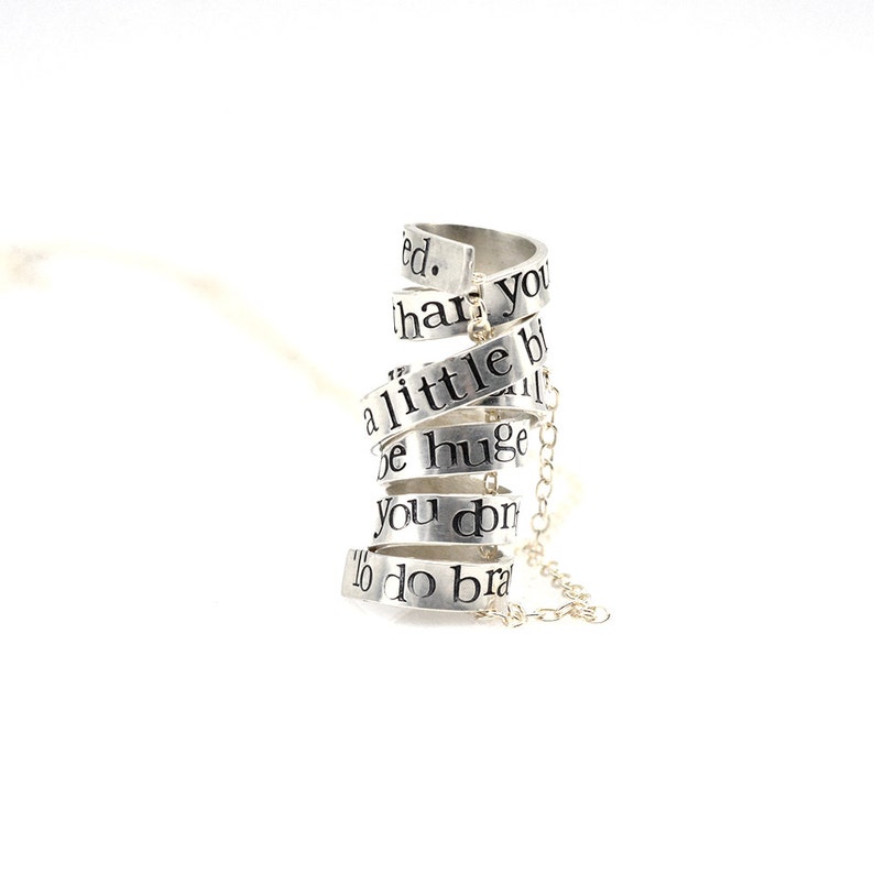 May include: Silver necklace with a spiral design featuring the words "You don't have to be huge to do brave things. A little bit of brave can change everything."