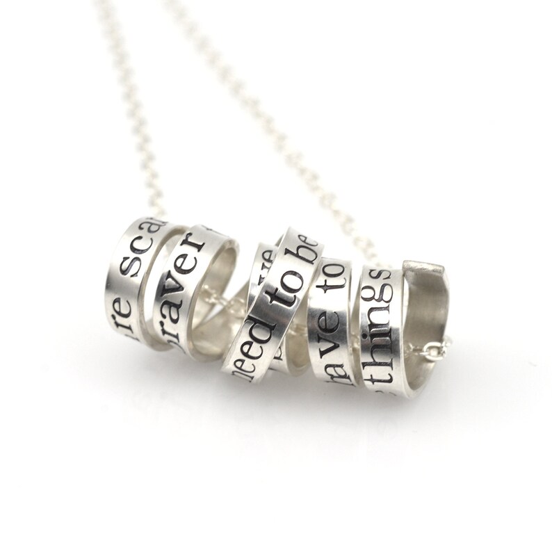 May include: Silver necklace with a spiral of rings, each engraved with a different word: "be", "brave", "need to be", "have to", "things", "re scared".