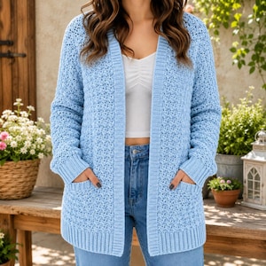 May include: A light blue open-front cardigan featuring a textured crochet knit pattern, long sleeves with ribbed cuffs, and two front patch pockets. The garment is worn over a white top and blue denim jeans, showcasing a consistent knit texture.
