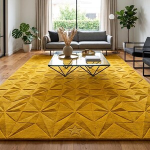 May include: A large rectangular area rug in a vibrant mustard yellow color featuring a raised geometric pattern of triangles and star shapes across the entire surface. The rug has a thick, textured pile and is laid flat on a wooden floor.